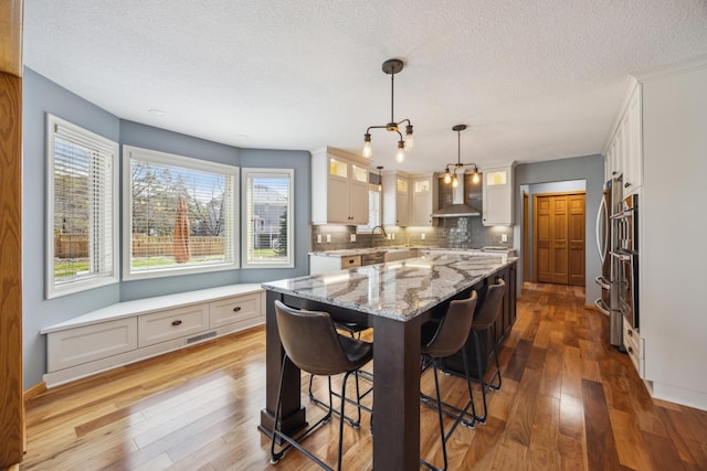 kitchen with wall chimney exhaust hood, a center island, a textured ceiling, and light wood finished floors