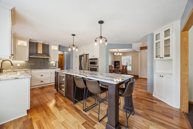 kitchen featuring wall chimney range hood, stainless steel appliances, wine cooler, and light wood-style floors