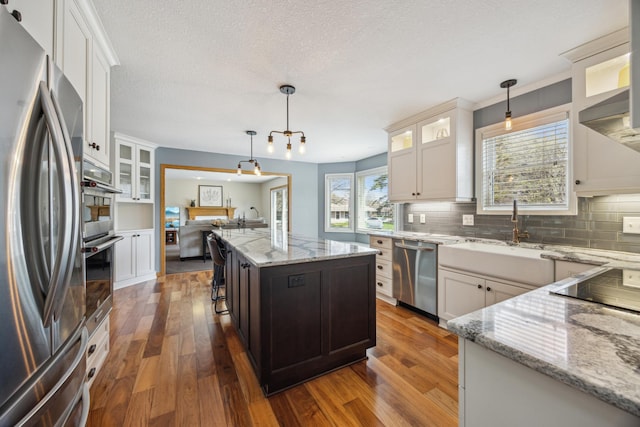 kitchen featuring dark wood finished floors, a sink, light stone countertops, tasteful backsplash, and appliances with stainless steel finishes