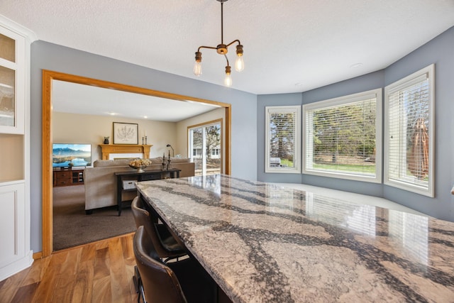 kitchen with hanging light fixtures, stone countertops, wood finished floors, and a textured ceiling