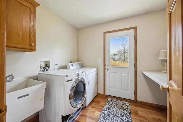 washroom featuring light wood finished floors, a sink, independent washer and dryer, cabinet space, and a textured ceiling