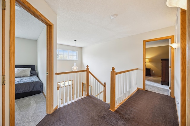 hall featuring carpet floors, an upstairs landing, a textured ceiling, and baseboards