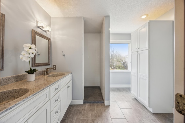 full bathroom featuring recessed lighting, double vanity, a textured ceiling, and a sink