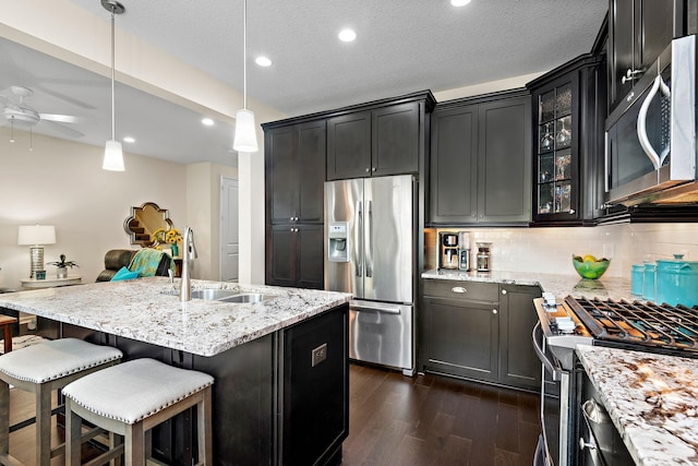 kitchen with pendant lighting, sink, appliances with stainless steel finishes, light stone countertops, and dark hardwood / wood-style flooring