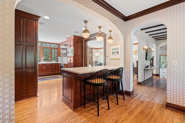 kitchen with pendant lighting, stainless steel microwave, kitchen peninsula, crown molding, and light wood-type flooring