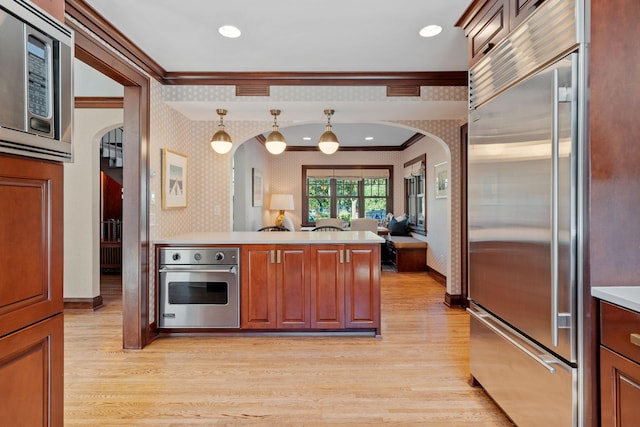 kitchen featuring crown molding, built in appliances, decorative light fixtures, kitchen peninsula, and light wood-type flooring