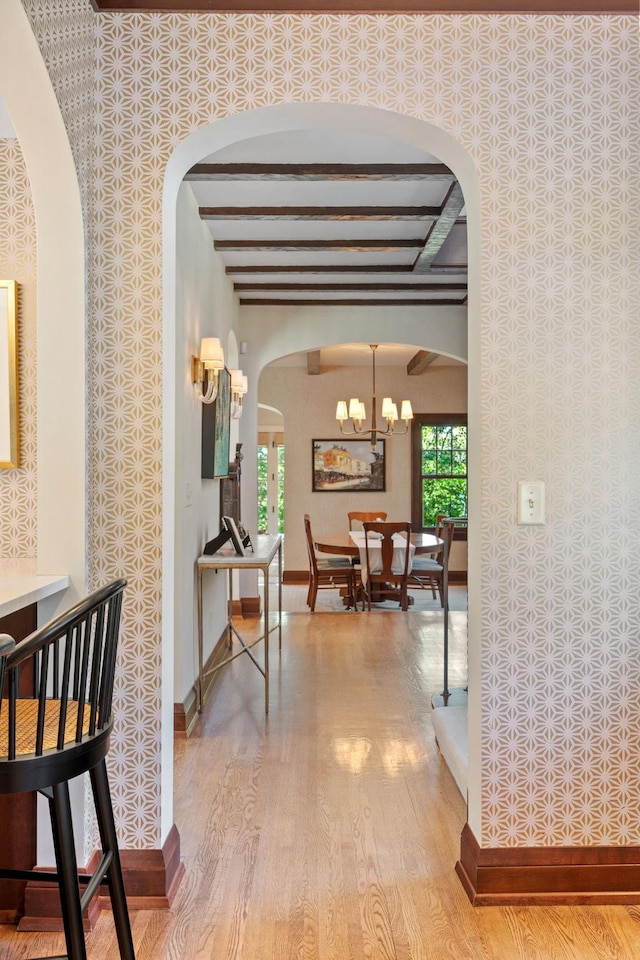 hallway with an inviting chandelier, light hardwood / wood-style flooring, and beamed ceiling