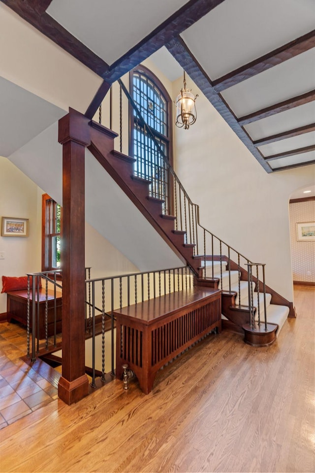 staircase with beamed ceiling, a chandelier, hardwood / wood-style floors, and decorative columns