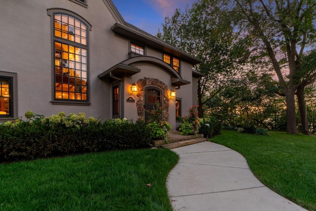 exterior entry at dusk featuring a lawn