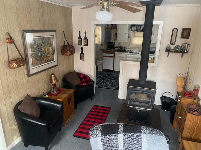 living room with wood walls, ceiling fan, and a wood stove