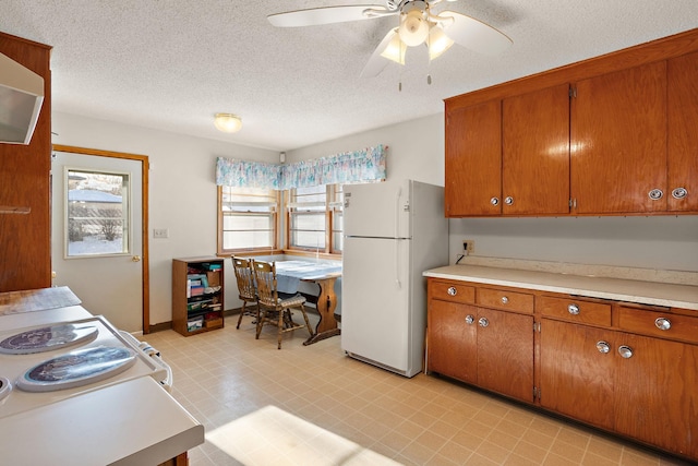 kitchen with freestanding refrigerator, a ceiling fan, brown cabinets, and light countertops
