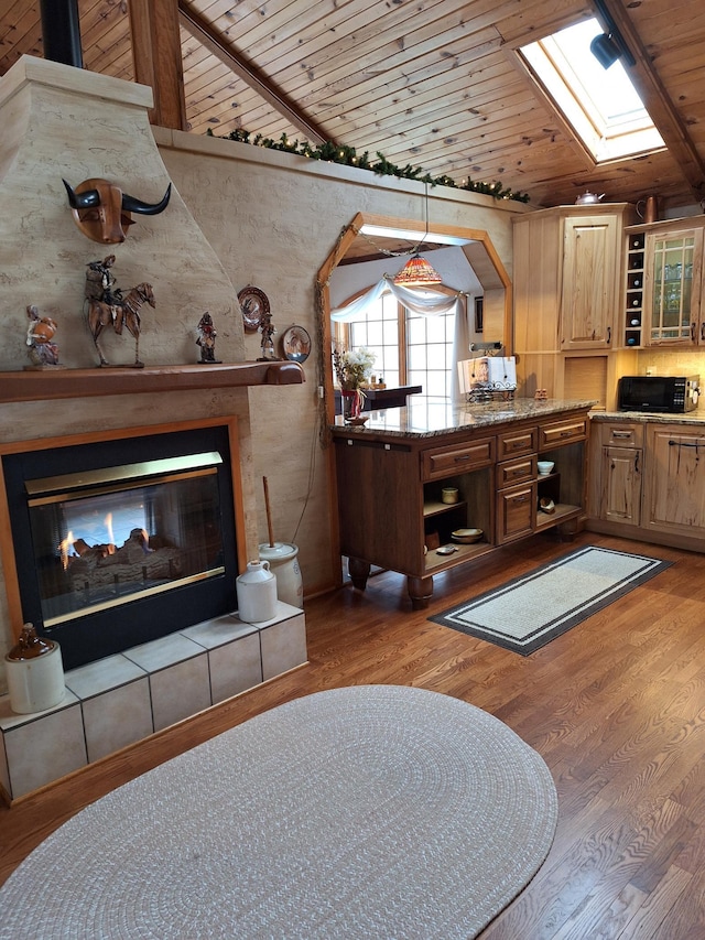 living area with vaulted ceiling with skylight, wood ceiling, a tiled fireplace, and light wood finished floors