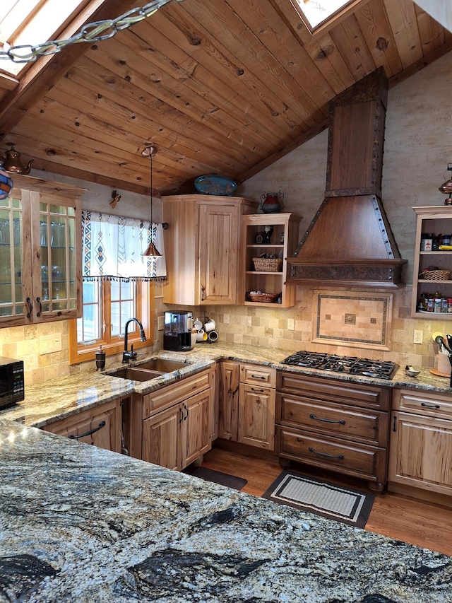 kitchen with light stone countertops, premium range hood, stainless steel gas stovetop, and lofted ceiling with skylight