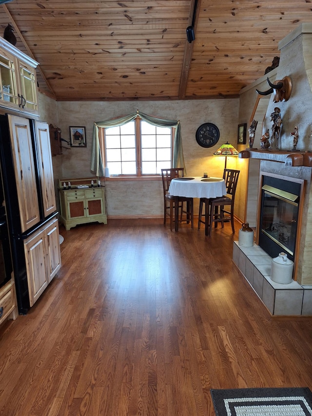 dining area featuring dark wood-type flooring, a tile fireplace, wooden ceiling, and vaulted ceiling with beams