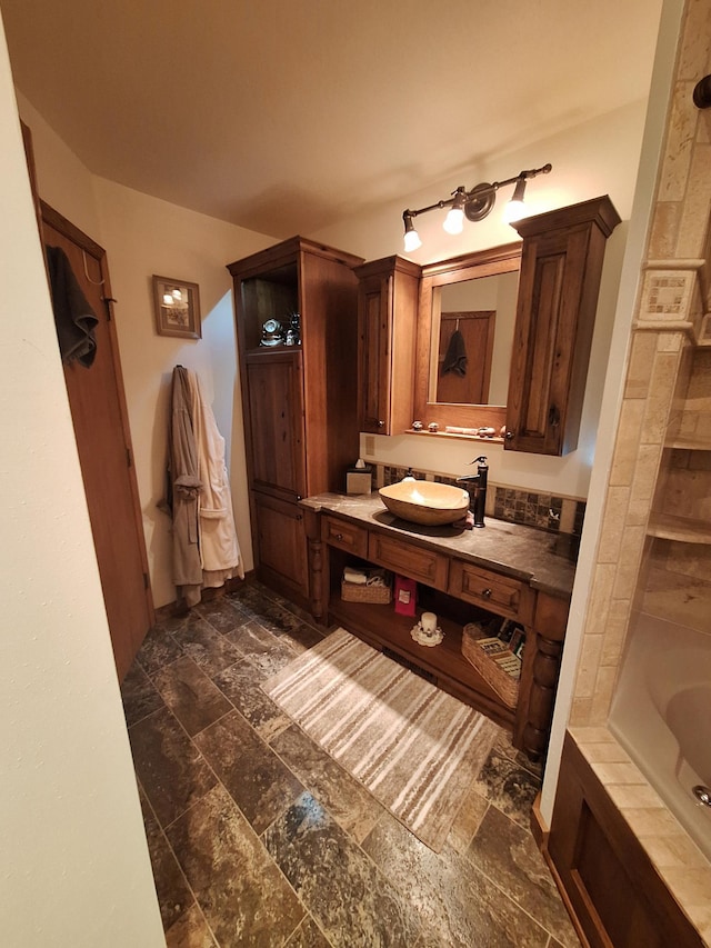 bathroom featuring stone tile floors, a bath, and vanity