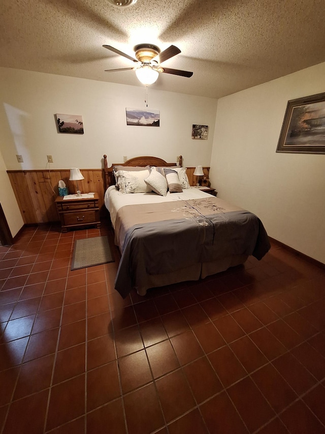 bedroom with wooden walls, wainscoting, dark tile patterned floors, and a textured ceiling