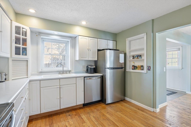 kitchen with sink, stainless steel appliances, a textured ceiling, white cabinets, and light wood-type flooring