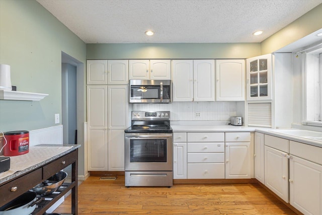 kitchen with sink, a textured ceiling, light hardwood / wood-style flooring, appliances with stainless steel finishes, and white cabinets