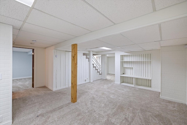 basement with brick wall, light colored carpet, and a paneled ceiling