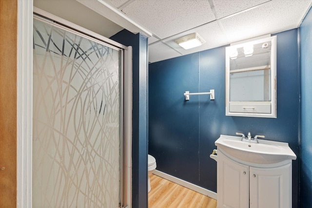 bathroom featuring hardwood / wood-style flooring, a paneled ceiling, vanity, a shower with shower door, and toilet