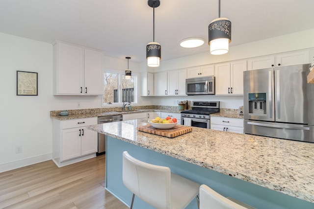 kitchen with stainless steel appliances, a breakfast bar, a sink, white cabinets, and light stone countertops