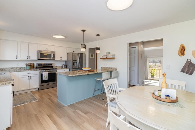 kitchen with light stone counters, stainless steel appliances, a peninsula, white cabinetry, and light wood-style floors