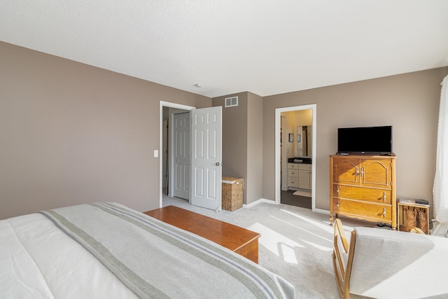 bedroom with baseboards, ensuite bath, visible vents, and light colored carpet