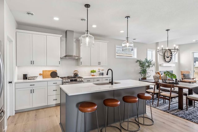 10974 37th St N, Lake Elmo, MN 55042 - kitchen featuring a kitchen island with sink, wall chimney range hood, light wood-type flooring, stainless steel range with gas cooktop, and a sink