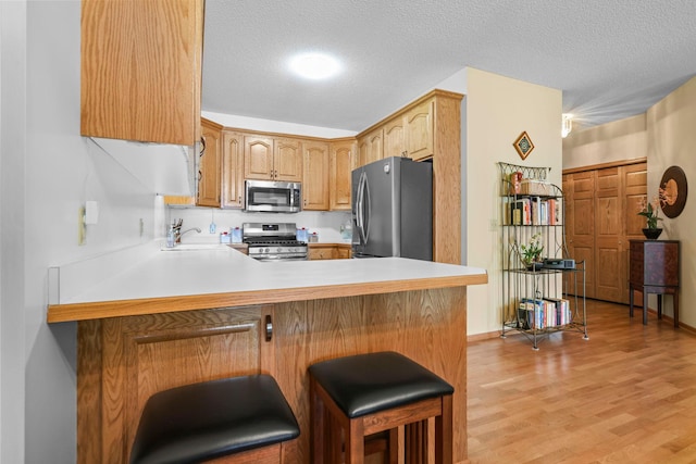 11030 Mississippi Blvd NW Unit 221, Coon Rapids, MN 55433 - kitchen featuring appliances with stainless steel finishes, a peninsula, light wood-style flooring, light countertops, and a textured ceiling