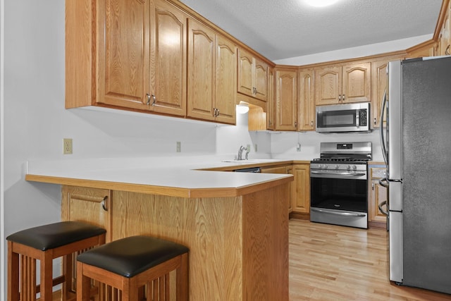 11030 Mississippi Blvd NW Unit 221, Coon Rapids, MN 55433 - kitchen with appliances with stainless steel finishes, a peninsula, light wood-style floors, a breakfast bar, and a textured ceiling