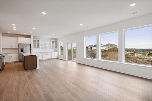 kitchen with light hardwood / wood-style flooring, white cabinetry, stove, stainless steel refrigerator with ice dispenser, and an island with sink