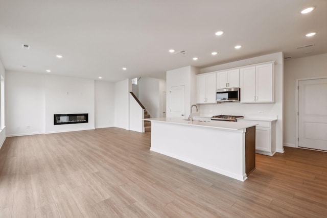 kitchen with sink, a kitchen island with sink, stove, light hardwood / wood-style floors, and white cabinets