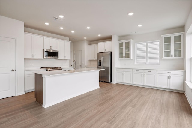 kitchen with sink, appliances with stainless steel finishes, a kitchen island with sink, white cabinetry, and light hardwood / wood-style floors