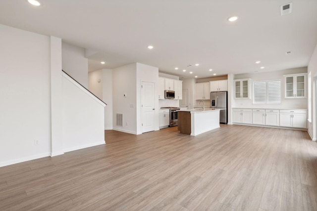 kitchen with sink, light hardwood / wood-style flooring, a kitchen island with sink, stainless steel appliances, and white cabinets