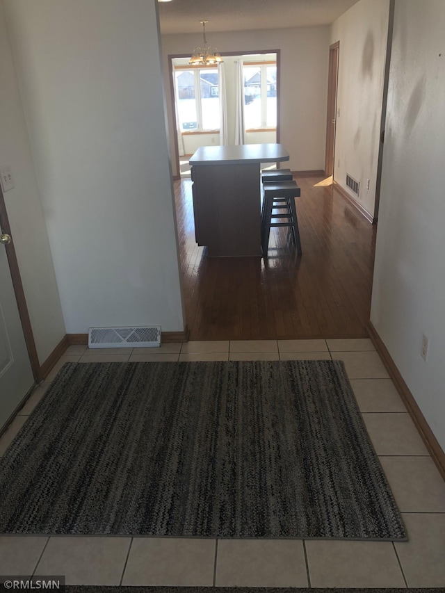 corridor featuring an inviting chandelier, visible vents, and tile patterned floors