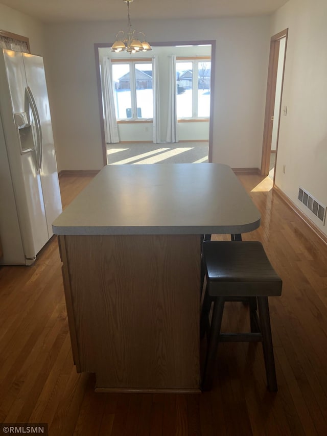 kitchen featuring wood finished floors, visible vents, a kitchen island, an inviting chandelier, and white fridge with ice dispenser