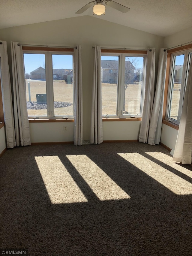 spare room featuring dark colored carpet, lofted ceiling, and a healthy amount of sunlight