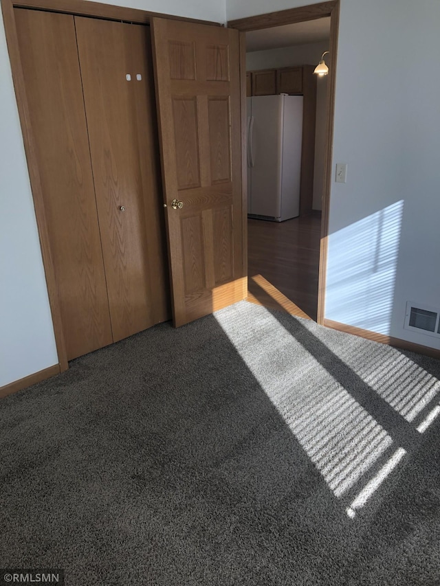 unfurnished bedroom featuring baseboards, visible vents, freestanding refrigerator, a closet, and carpet flooring