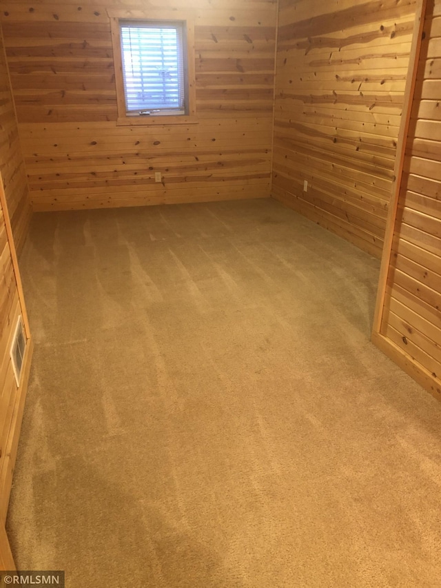 carpeted empty room featuring wooden walls and visible vents