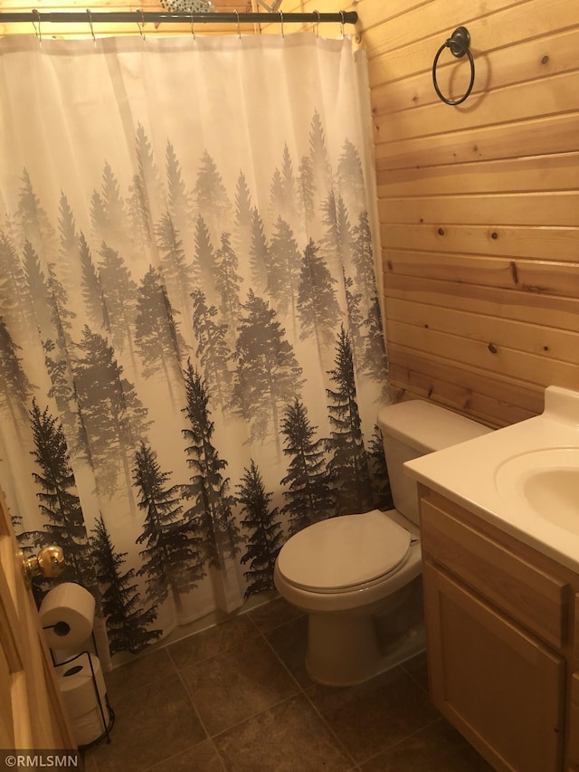 full bath with tile patterned floors, wood walls, toilet, and vanity