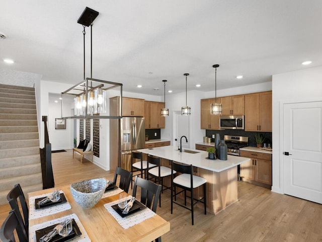 kitchen with pendant lighting, sink, light hardwood / wood-style flooring, appliances with stainless steel finishes, and an island with sink