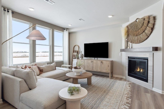 living room featuring plenty of natural light, a tiled fireplace, and light wood-type flooring