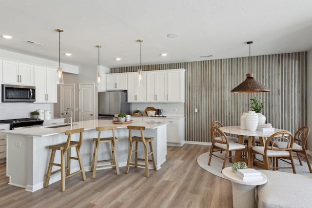 kitchen with sink, an island with sink, pendant lighting, stainless steel appliances, and white cabinets