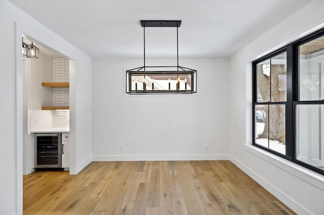 unfurnished dining area with wine cooler, light wood-style flooring, visible vents, baseboards, and a bar