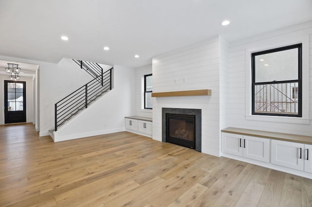 unfurnished living room featuring baseboards, a glass covered fireplace, stairs, light wood-style floors, and recessed lighting