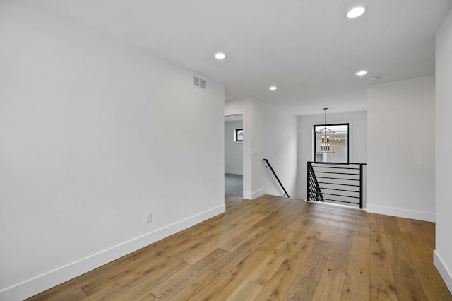 empty room with a notable chandelier, recessed lighting, visible vents, light wood-style flooring, and baseboards