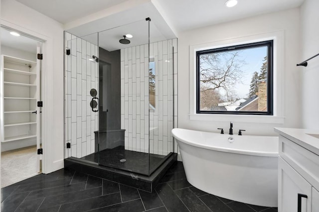 bathroom with a walk in closet, a shower stall, vanity, a freestanding tub, and tile patterned floors