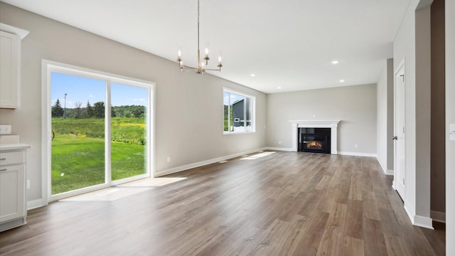 7472 170th Ave NW, Ramsey, MN 55303 - unfurnished living room featuring an inviting chandelier, a wealth of natural light, a glass covered fireplace, and wood finished floors