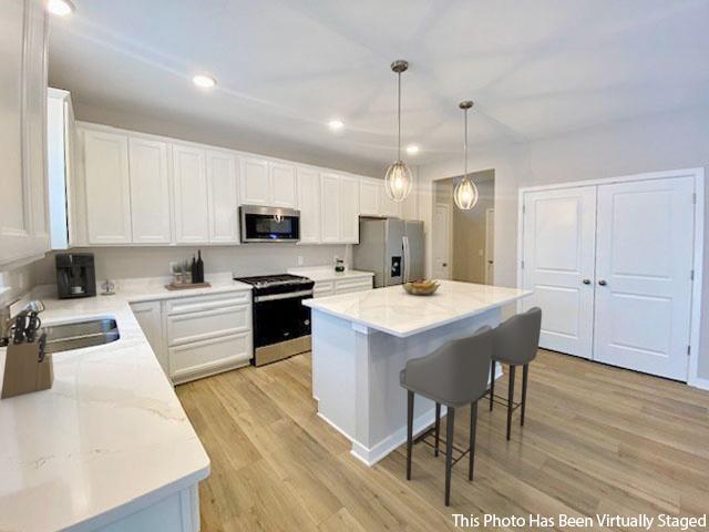 kitchen featuring a breakfast bar area, stainless steel appliances, white cabinets, a sink, and light wood-type flooring