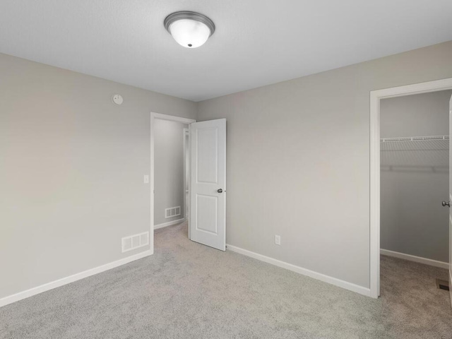 unfurnished bedroom with a spacious closet, light colored carpet, and a closet